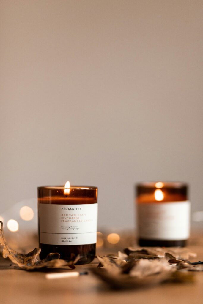 Two lit candles surrounded by dry autumn leaves creating a warm cozy atmosphere with soft golden light