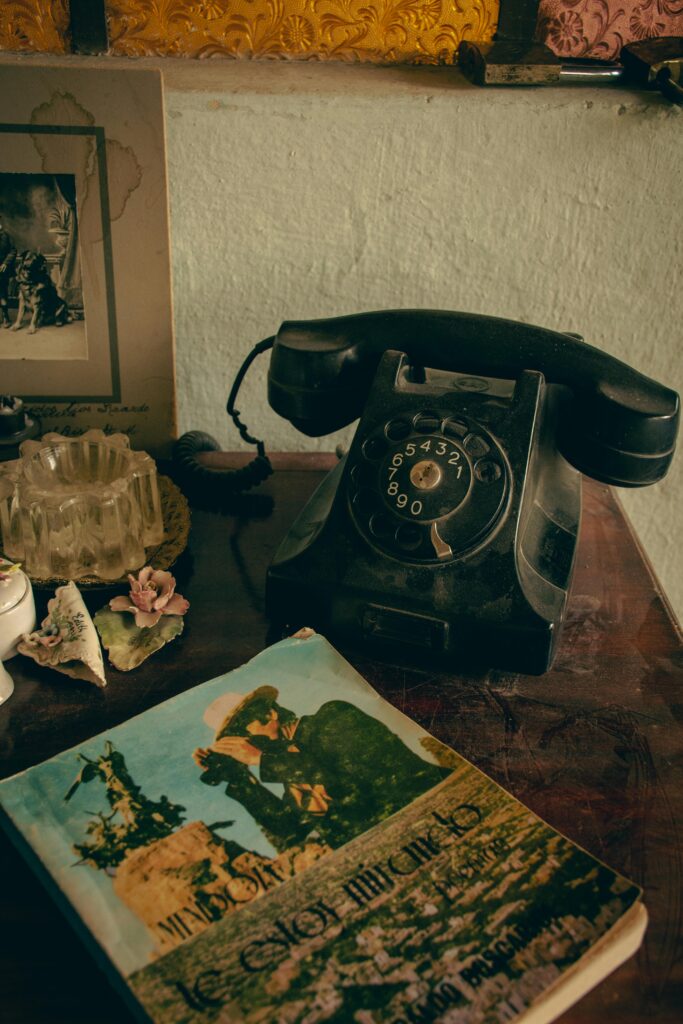 Vintage black rotary telephone on a wooden table beside old photographs and decorative objects in warm moody lighting.