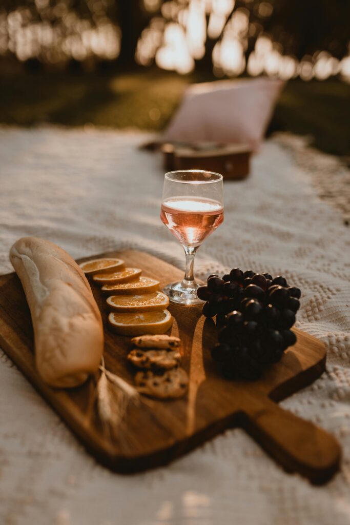Elegant outdoor picnic setup with a charcuterie board, champagne glasses, cookies, fresh bread, oranges, and blueberries arranged in a cozy aesthetic setting.