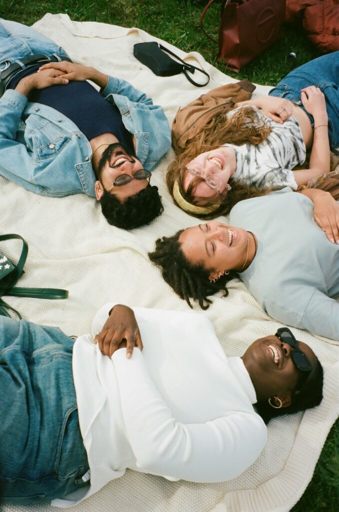 Friends laughing together on a picnic blanket during a cozy afternoon, representing the small human moments that make life softer and happier.