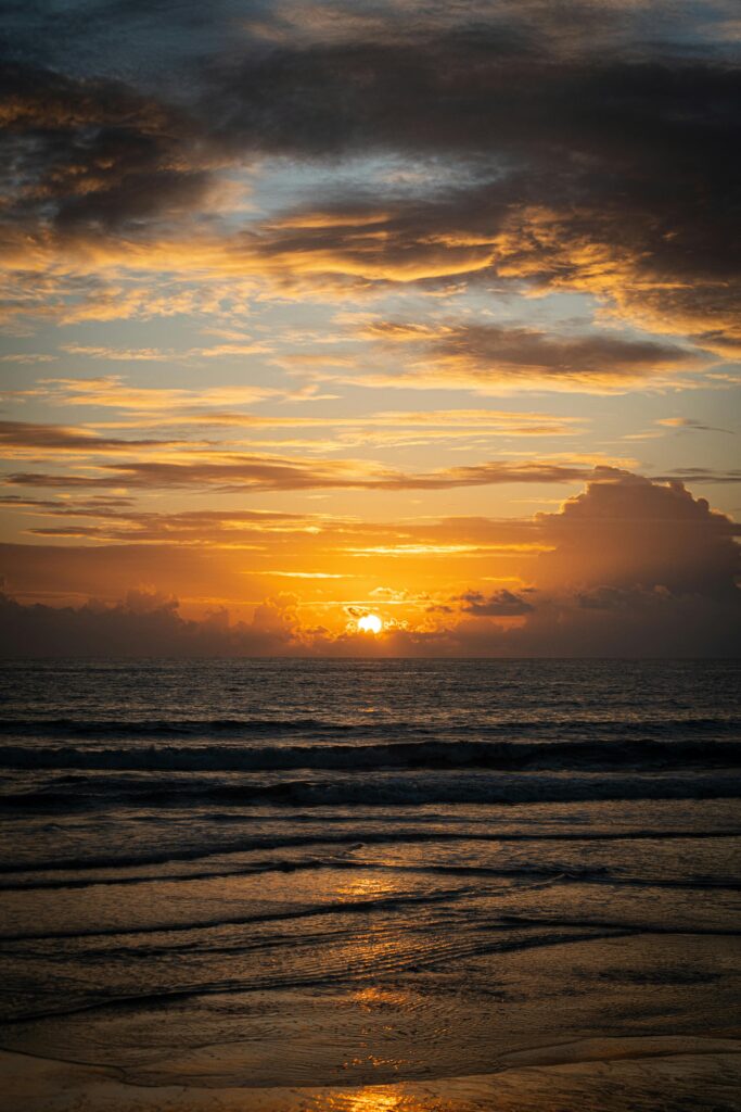 Golden sunset over ocean waves with dramatic clouds reflecting warm light on the water.