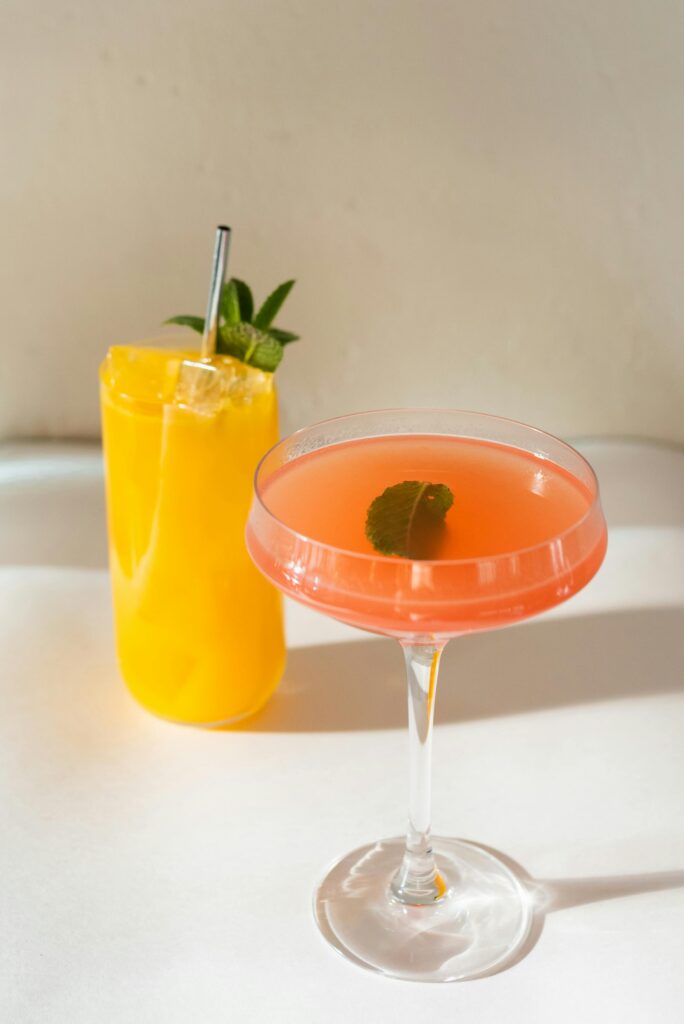 Pink and yellow aesthetic drinks in elegant glasses with sunlight reflecting on a white table.