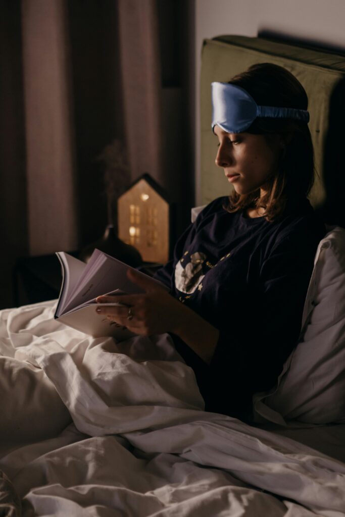 Girl reading a book in bed at night with warm dim lighting and silk sleep mask