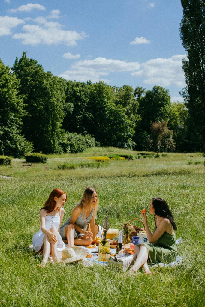 Three girls having a picnic in a sunny green field with aesthetic summer vibes.