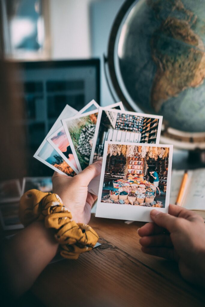 A cozy vintage-inspired aesthetic image featuring scattered polaroid photographs with a globe in the background, warm lighting, nostalgic decor, and soft earthy tones creating a dreamy slow living atmosphere.
