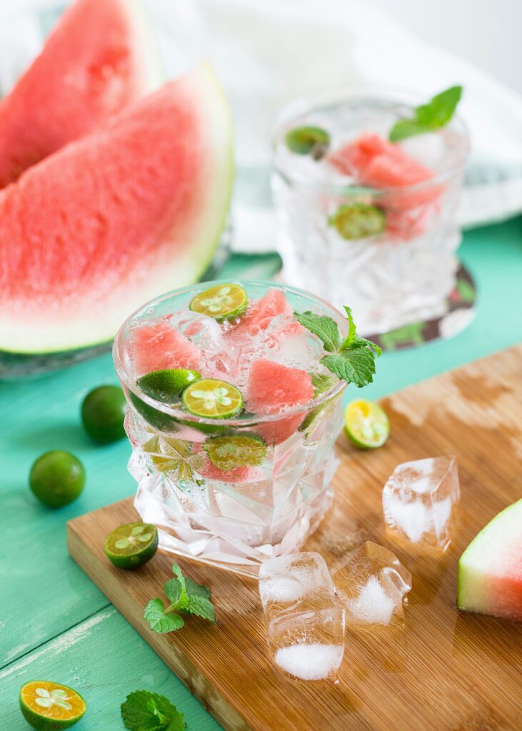 A refreshing watermelon drink surrounded by watermelon slices, ice cubes, and fresh limes in warm natural lighting, creating a bright summer aesthetic with cozy and vibrant tones.