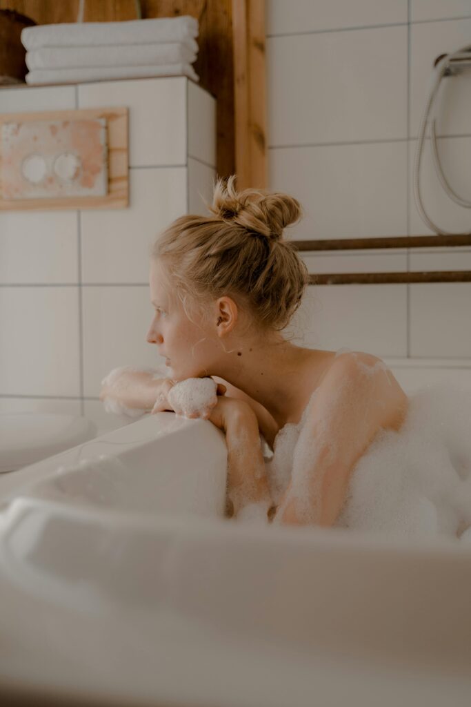 A woman relaxing in a bubble bath in a cozy bathroom with soft neutral tones and peaceful lighting.