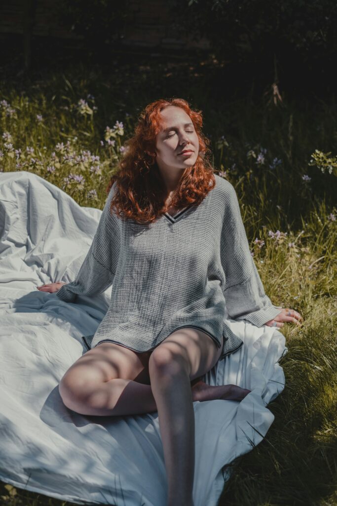 Person sitting on a blanket in a grassy field enjoying sunlight and a peaceful summer afternoon.