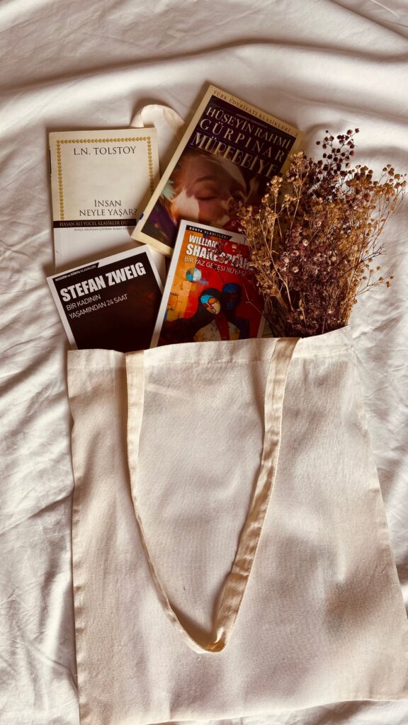 Canvas tote bag filled with books and dried flowers resting on a soft bed, representing an analog bag for reducing screen time and doomscrolling