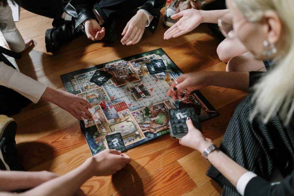 Group of people gathered around a board game on a wooden floor during game night.