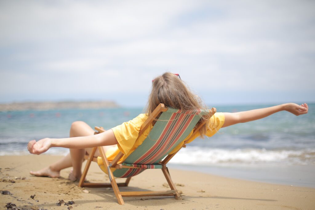 Person relaxing in a beach chair facing the ocean with arms stretched wide.