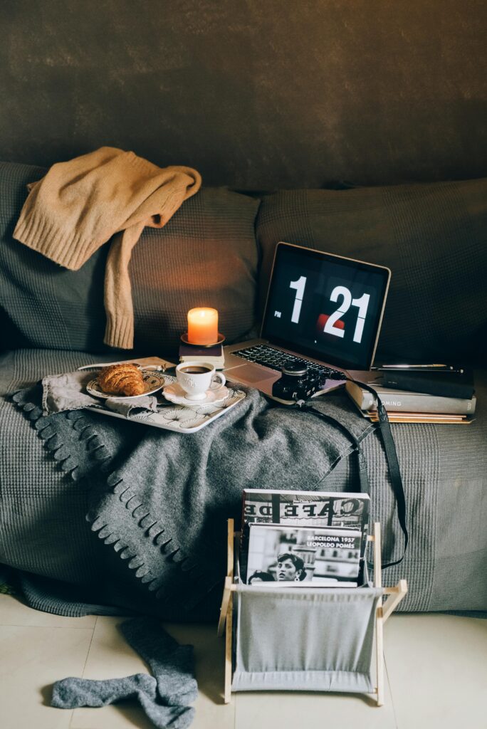 Cozy living room setup with a blanket, candle, coffee, books, and a couch creating a peaceful atmosphere.