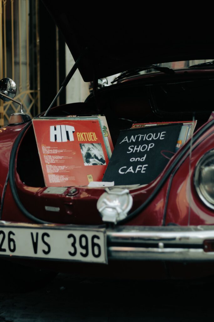 Vinyl records displayed in the trunk of a vintage car outside an antique shop and café.