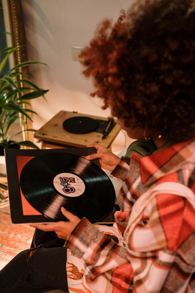 Person holding a vinyl record near a record player in a warm, cozy room.