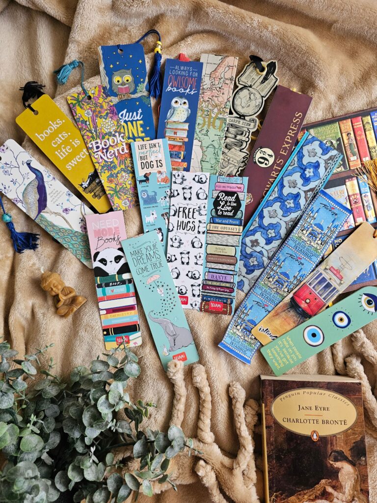 Colorful collection of decorative bookmarks spread across a cozy blanket beside books and greenery.