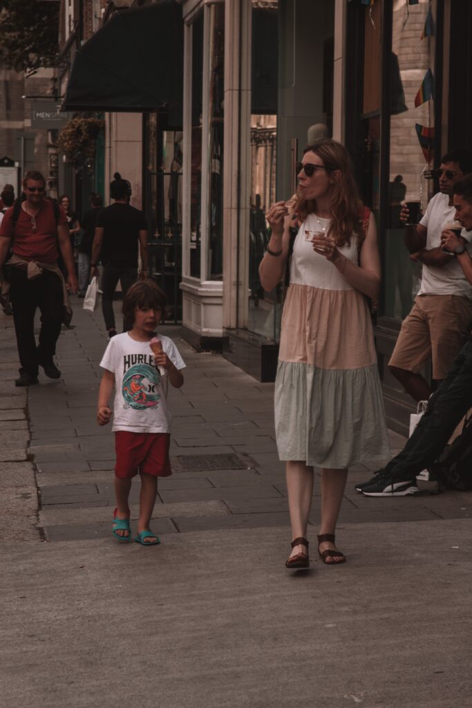 Woman and child enjoying ice cream while walking along a city street on a summer day.