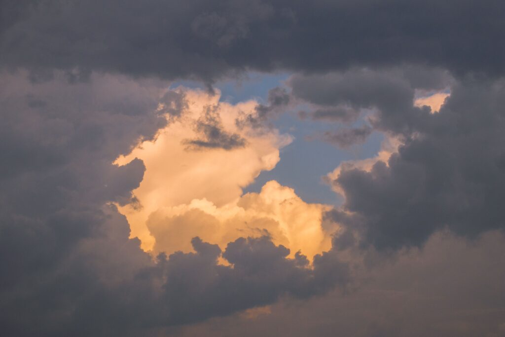 Dark storm clouds opening to reveal glowing golden clouds and blue sky, symbolizing hope, perspective, and light after darkness.