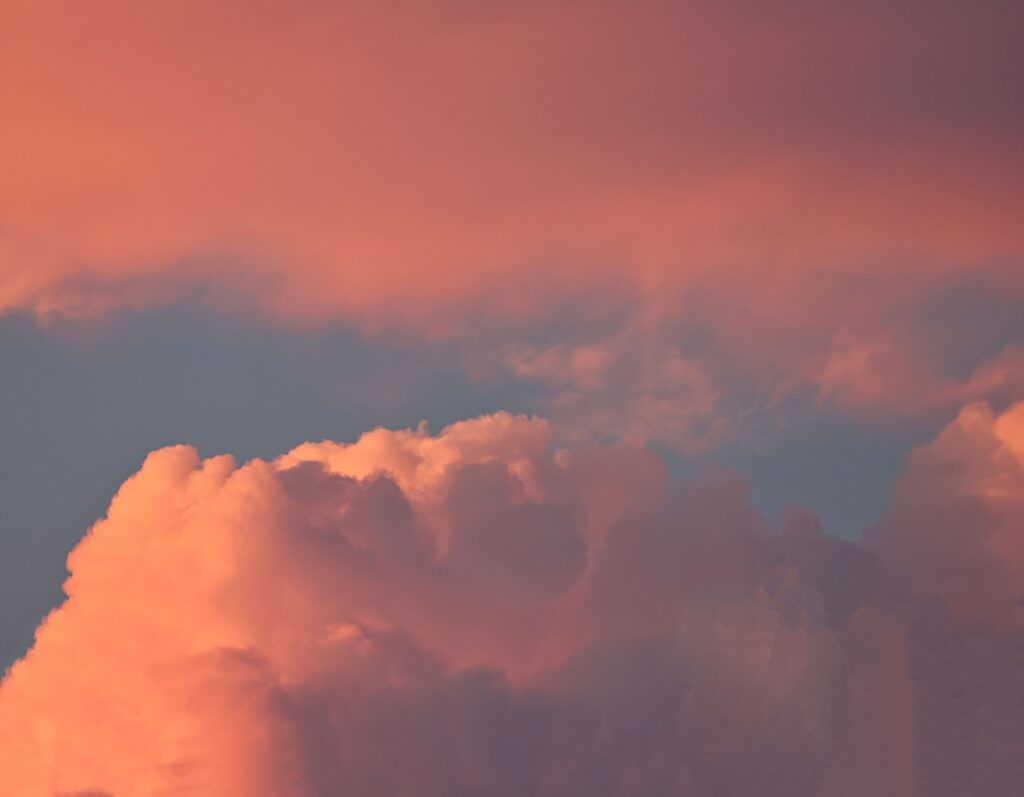 Soft pink and peach sunset clouds glowing in the evening sky with warm golden light creating a dreamy, peaceful atmosphere.