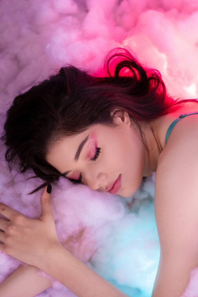 Woman sleeping on cotton candy symbolising clouds while she sees her wildest dreams in a calm and grounded manner