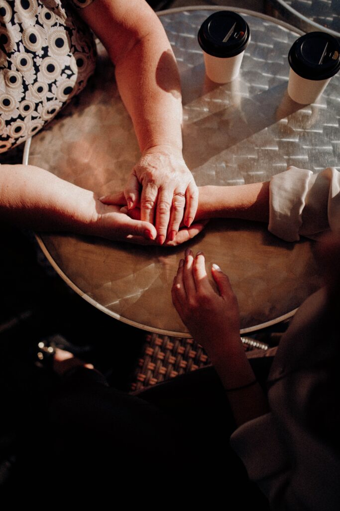 Several hands resting together across a café table, offering comfort, reassurance, and support during a shared moment.
