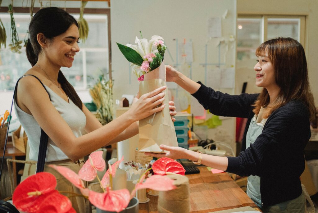 A kind wonan hands a bouquet of fresh flowers to a smiling customer, capturing a quiet moment of generosity and human connection.