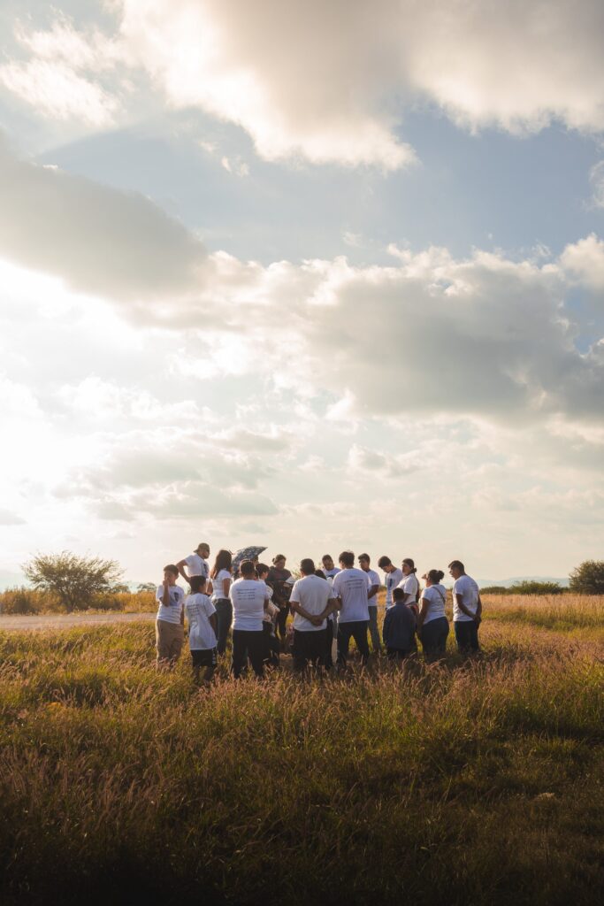 A group of people gathered in a sunlit field beneath dramatic clouds, symbolizing community, hope, and the invisible bonds that connect us.