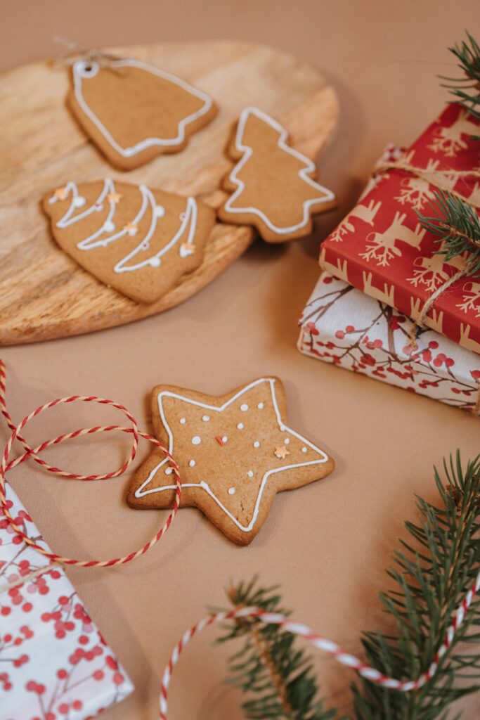 Decorated Christmas tree shaped cookies beside wrapped Christmas presents and evergreen branches on a cozy holiday table